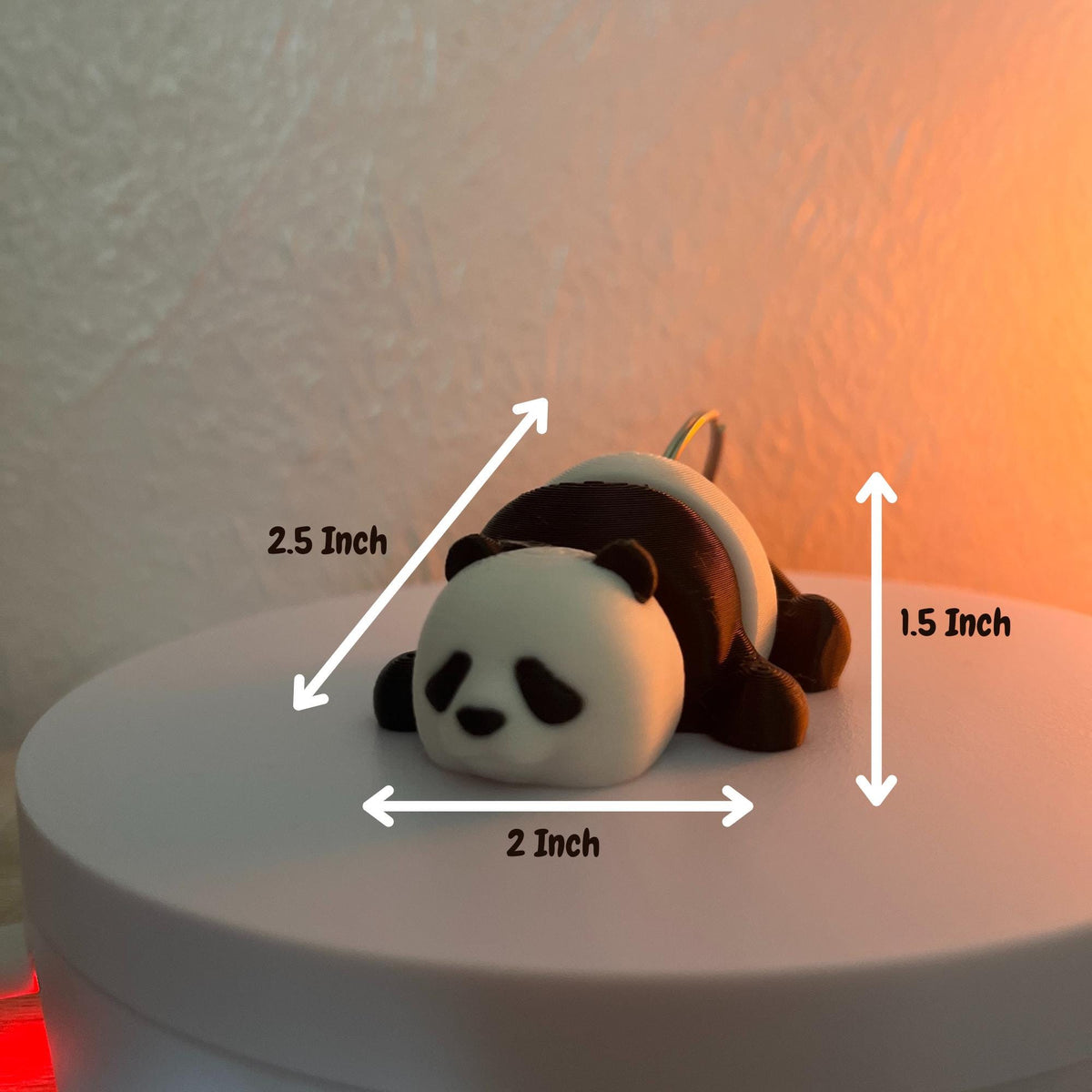 A small panda figurine, 2.5 inches long, 2 inches wide, and 1.5 inches tall, in a resting pose. The panda has a white head and body with black markings and small black ears. It is resting on a white surface.
