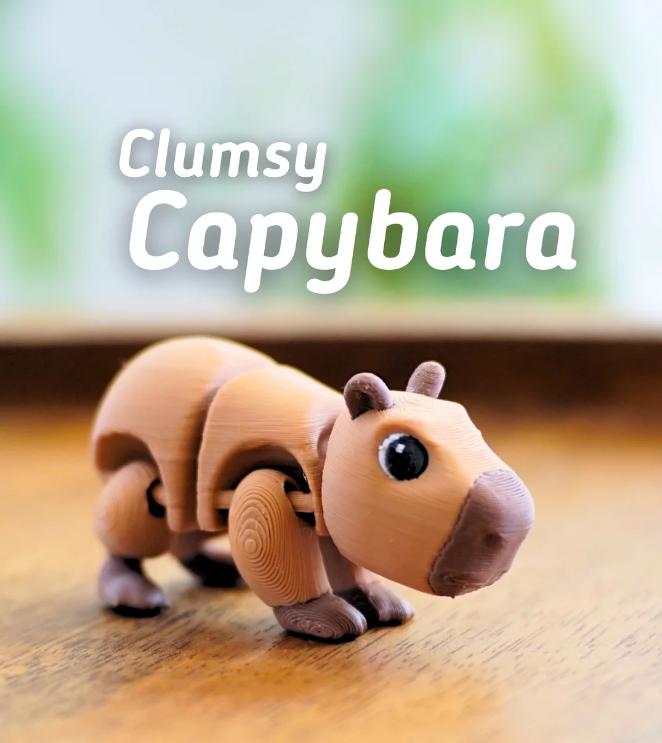 A tan, articulated capybara toy with the text "Clumsy Capybara". The toy has large, black eyes and a brown nose. The toy is made of a light brown material and is posed on a wooden surface.