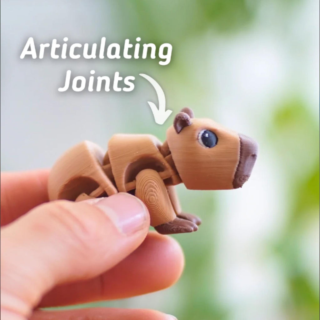 A brown articulated capybara toy with visible joints, held in a hand. The toy has a detailed design with a textured appearance. The text "Articulating Joints" is above the capybara.