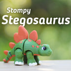 A green and orange Stegosaurus toy with the text "Stompy Stegosaurus". The toy has orange plates on its back and orange spots on its body. The dinosaur has white feet and a friendly expression.