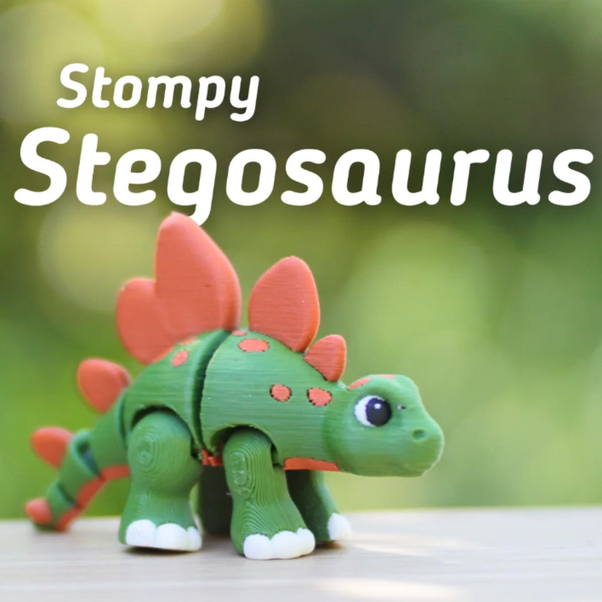 A green and orange Stegosaurus toy with the text "Stompy Stegosaurus". The toy has orange plates on its back and orange spots on its body. The dinosaur has white feet and a friendly expression.