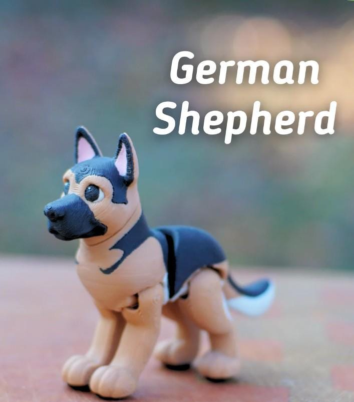 A small, articulated German Shepherd figurine featuring a tan and black color scheme with a black muzzle and pointed ears. The text "German Shepherd" is printed in white letters above the dog figure, which has visible joints.