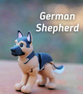 A small, articulated German Shepherd figurine featuring a tan and black color scheme with a black muzzle and pointed ears. The text "German Shepherd" is printed in white letters above the dog figure, which has visible joints.