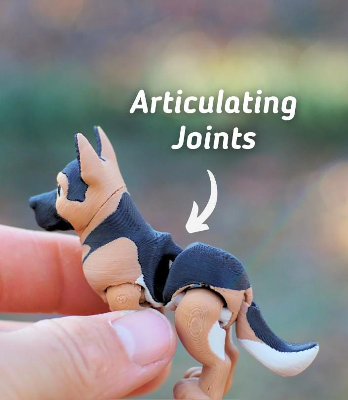 A small, articulated German Shepherd dog figurine featuring black and tan coloring with white accents on the tail. The figure displays visible joints at the midsection and limbs, with the text Articulating Joints and a white arrow.