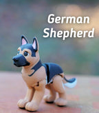 A small, articulated German Shepherd figurine featuring a tan and black color scheme with a textured surface. The dog has pointed ears, dark eyes, and a black muzzle. The text "German Shepherd" is displayed in white above the figure.